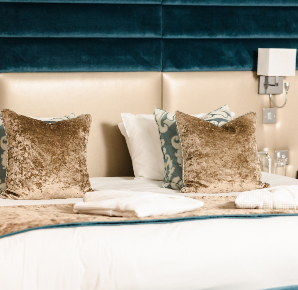 A neatly made hotel bed with plush pillows, a decorative headboard, and towels placed at the foot of the bed.