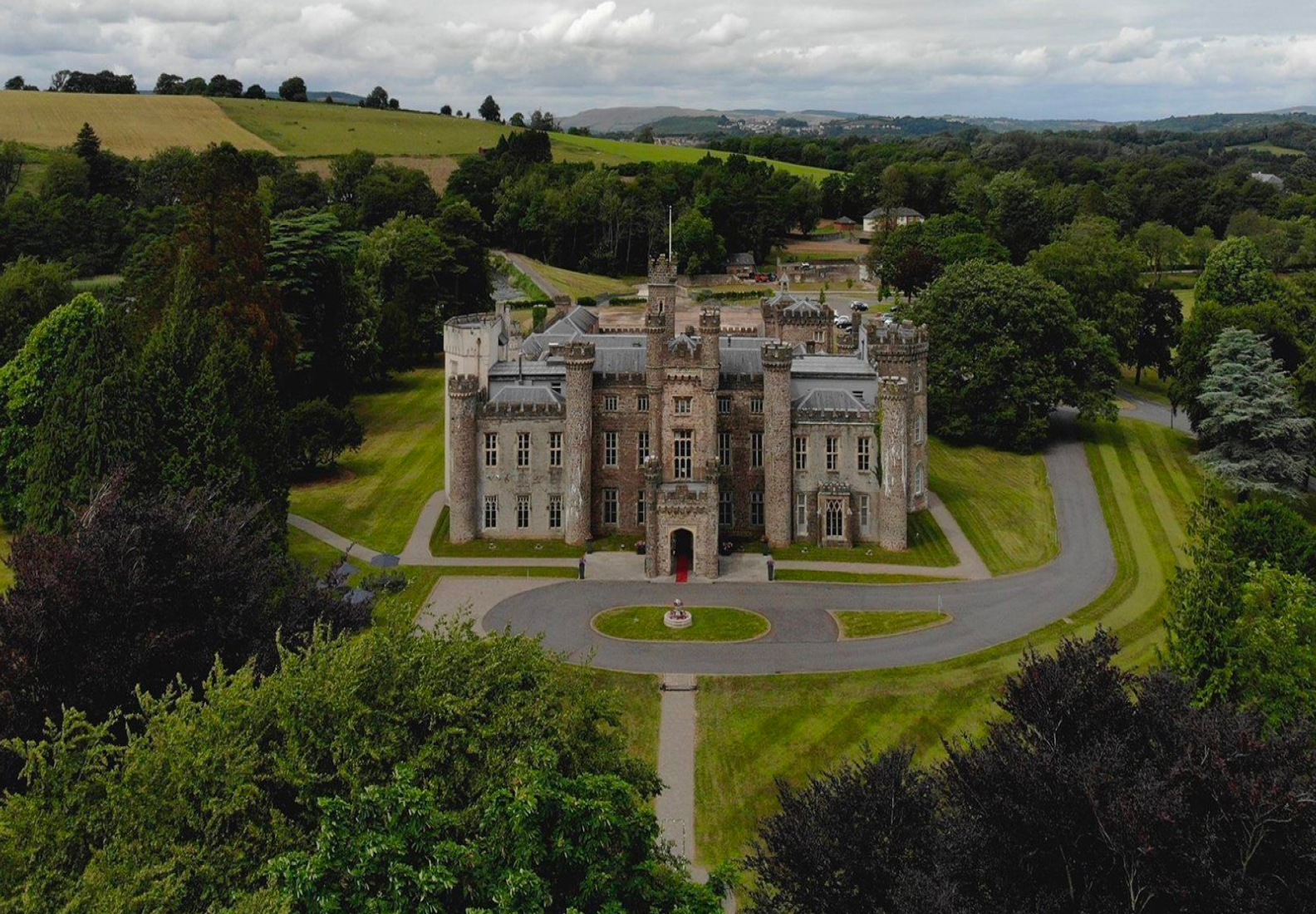 Aerial view of a large, historic castle surrounded by lush greenery and rolling hills.