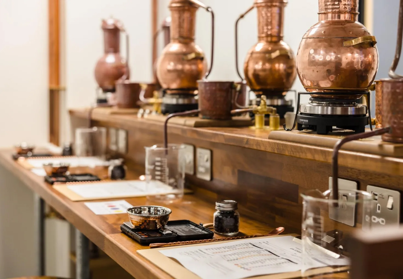 Copper distillation equipment and beakers line a wooden countertop in a laboratory setting.