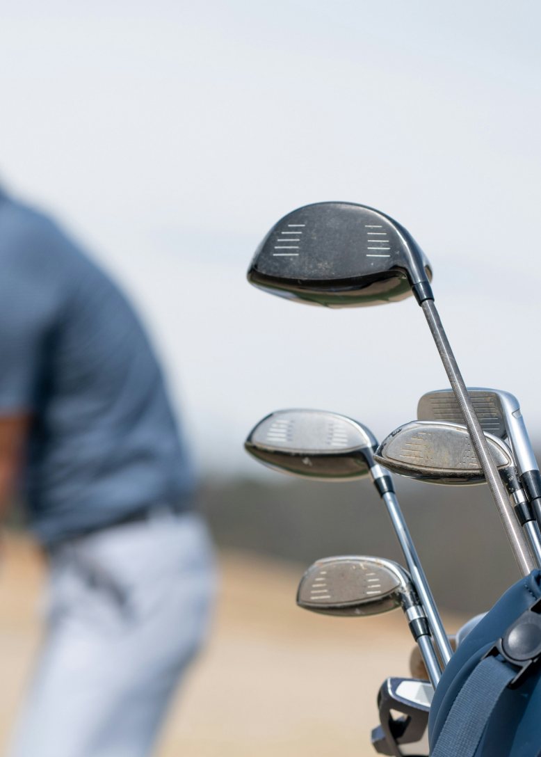 Golf clubs in a bag with a blurred person swinging in the background.