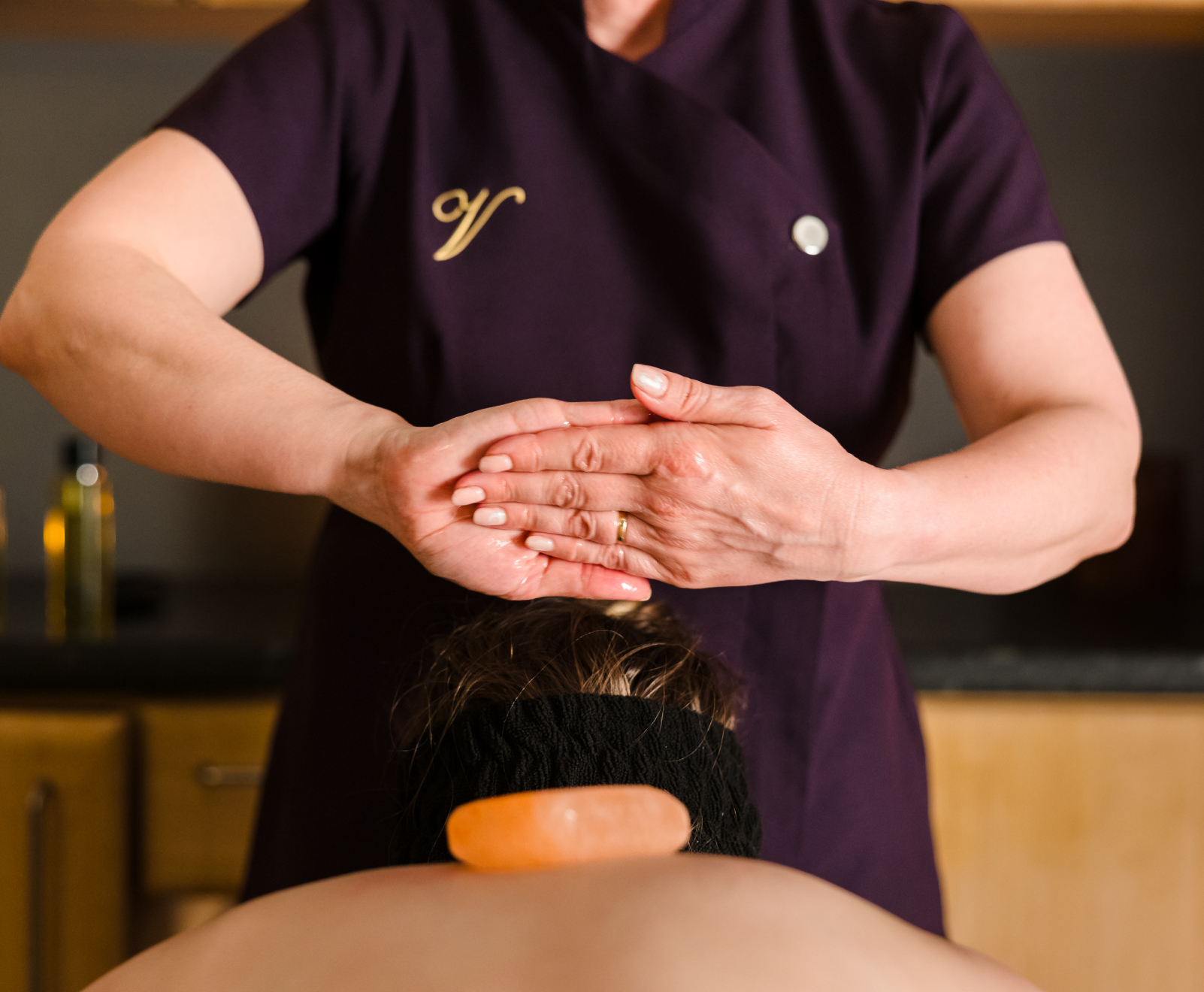 A person receiving a massage while lying face down. The massage therapist's hands are together, and there is a stone on the person's back.