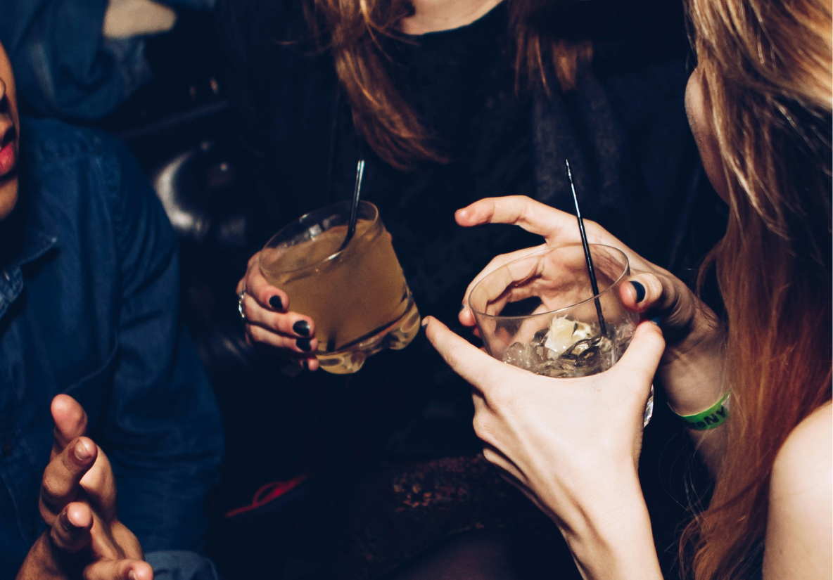 People holding drinks and gesturing while sitting together in a social setting.