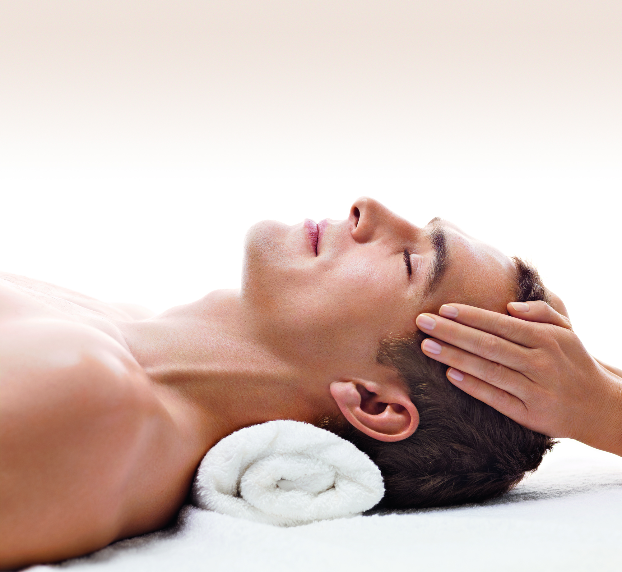 A person receiving a head massage while lying on their back, resting on a rolled towel.