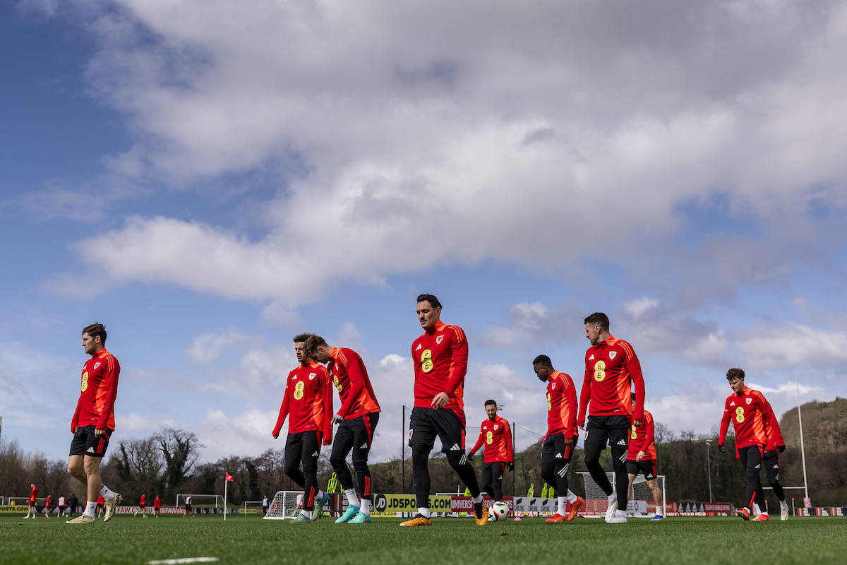 A soccer team in red uniforms trains on a green field under a cloudy sky.