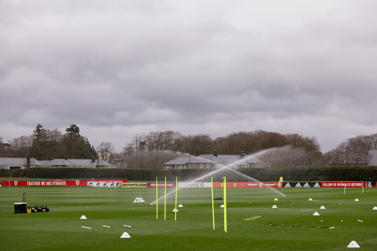 Soccer training field with cones, poles, and a ball cart under a cloudy sky, with sprinklers watering the grass.