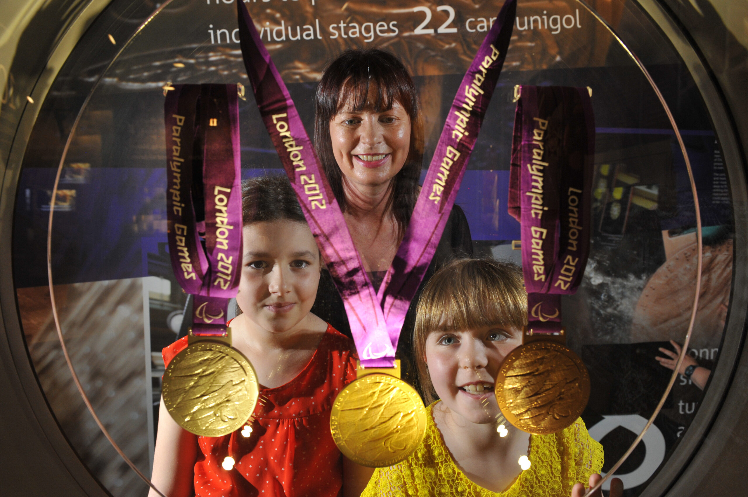 Two children and a woman pose with three London 2012 Paralympic gold medals hanging in front of them.