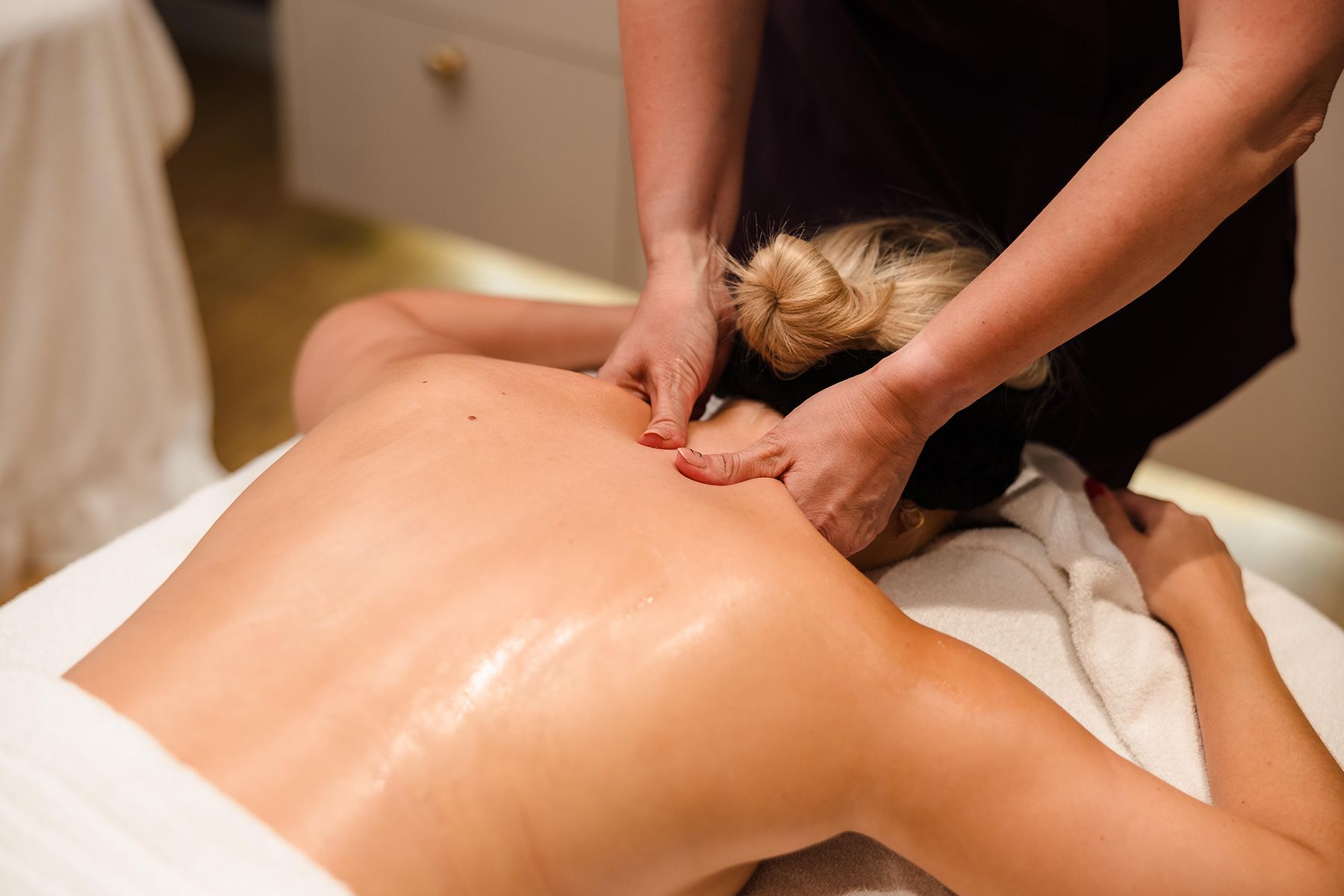 A person receiving a back massage with hands applying pressure near the shoulders.