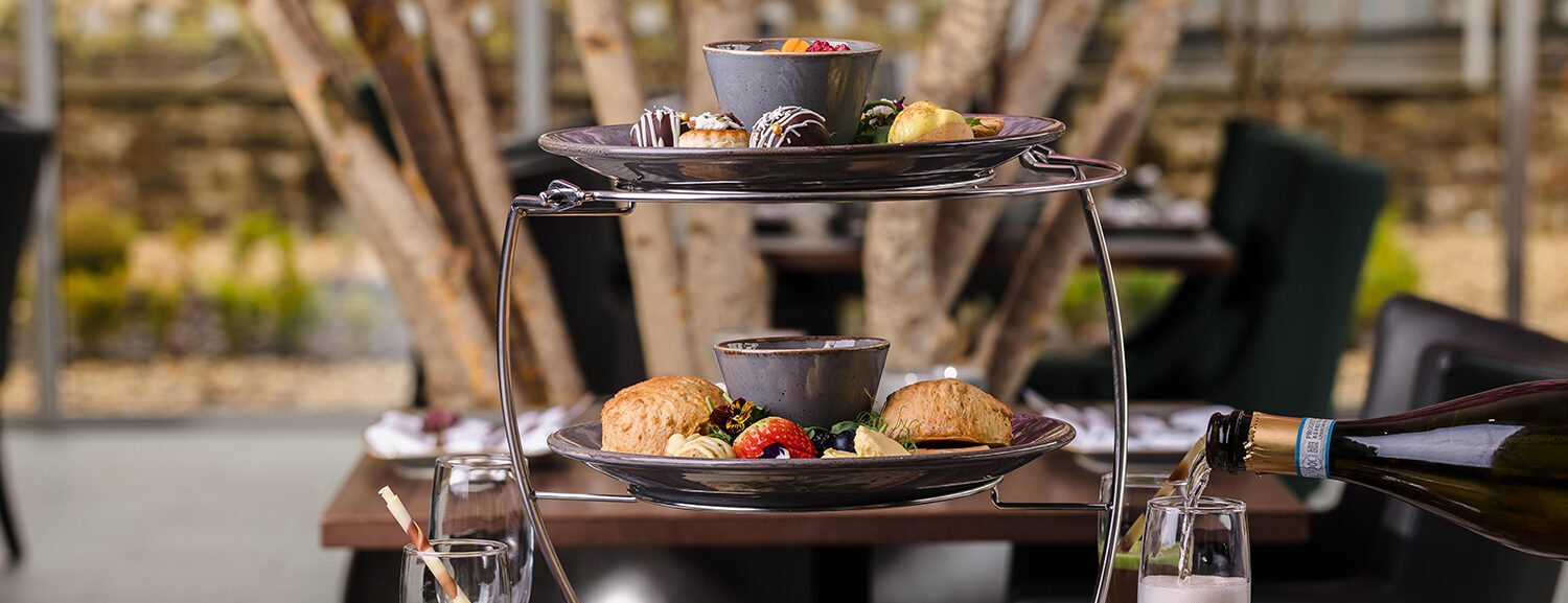 Two-tiered tray with assorted pastries and desserts alongside a bottle pouring sparkling drink into a glass on a dining table.