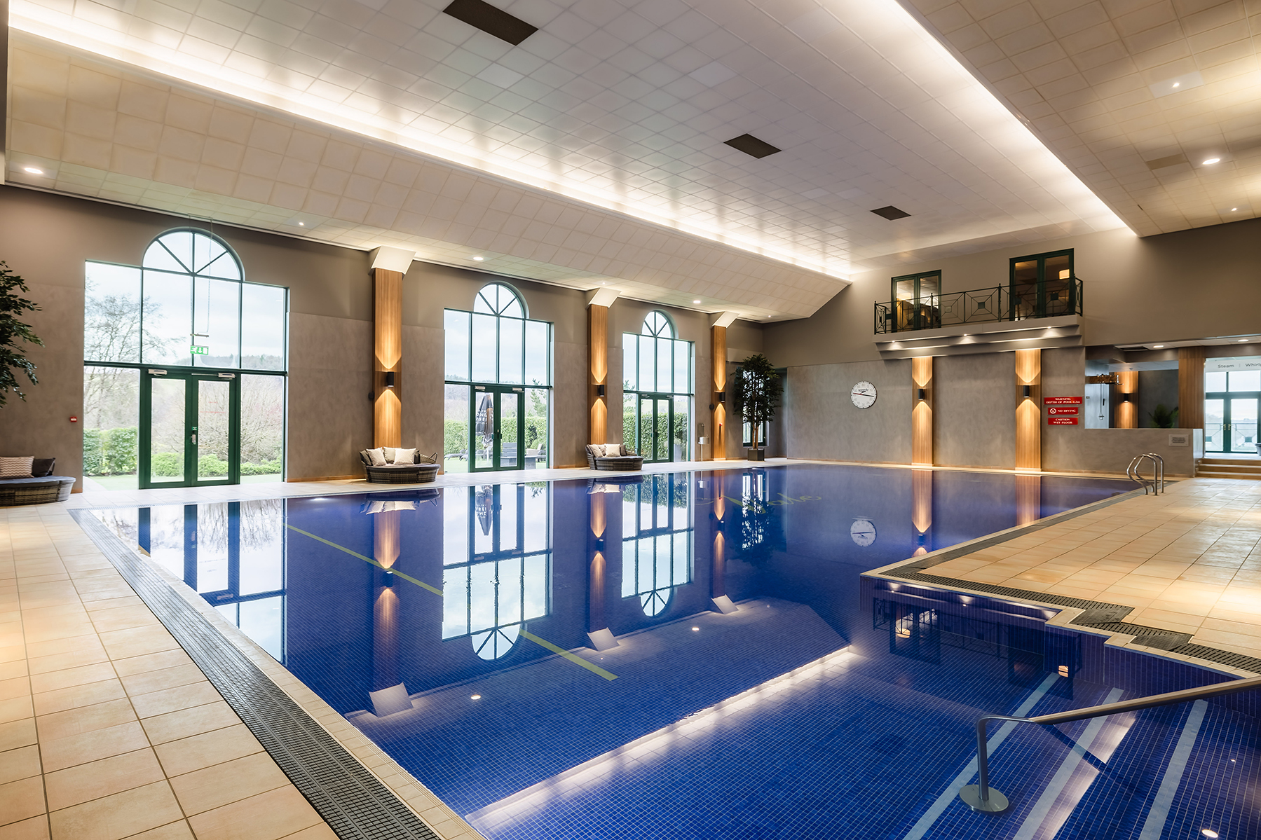 Indoor swimming pool with large windows, vaulted ceiling, and lounge chairs on the side.