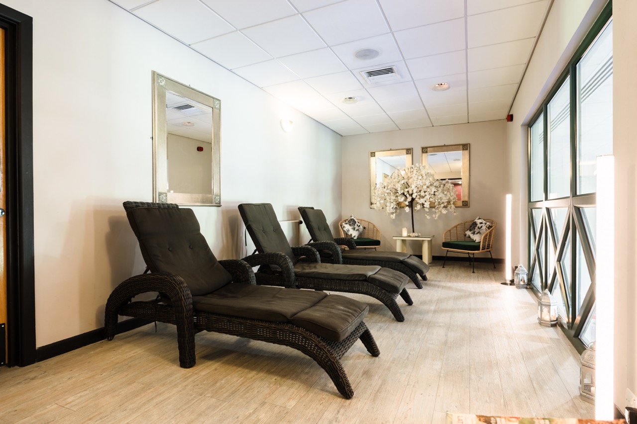 A relaxing spa lounge with wicker recliners, decorative mirrors, and a floral arrangement on a wooden floor.