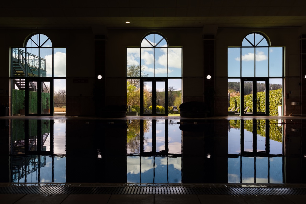 Indoor pool area with large floor-to-ceiling arched windows casting reflections on the water.