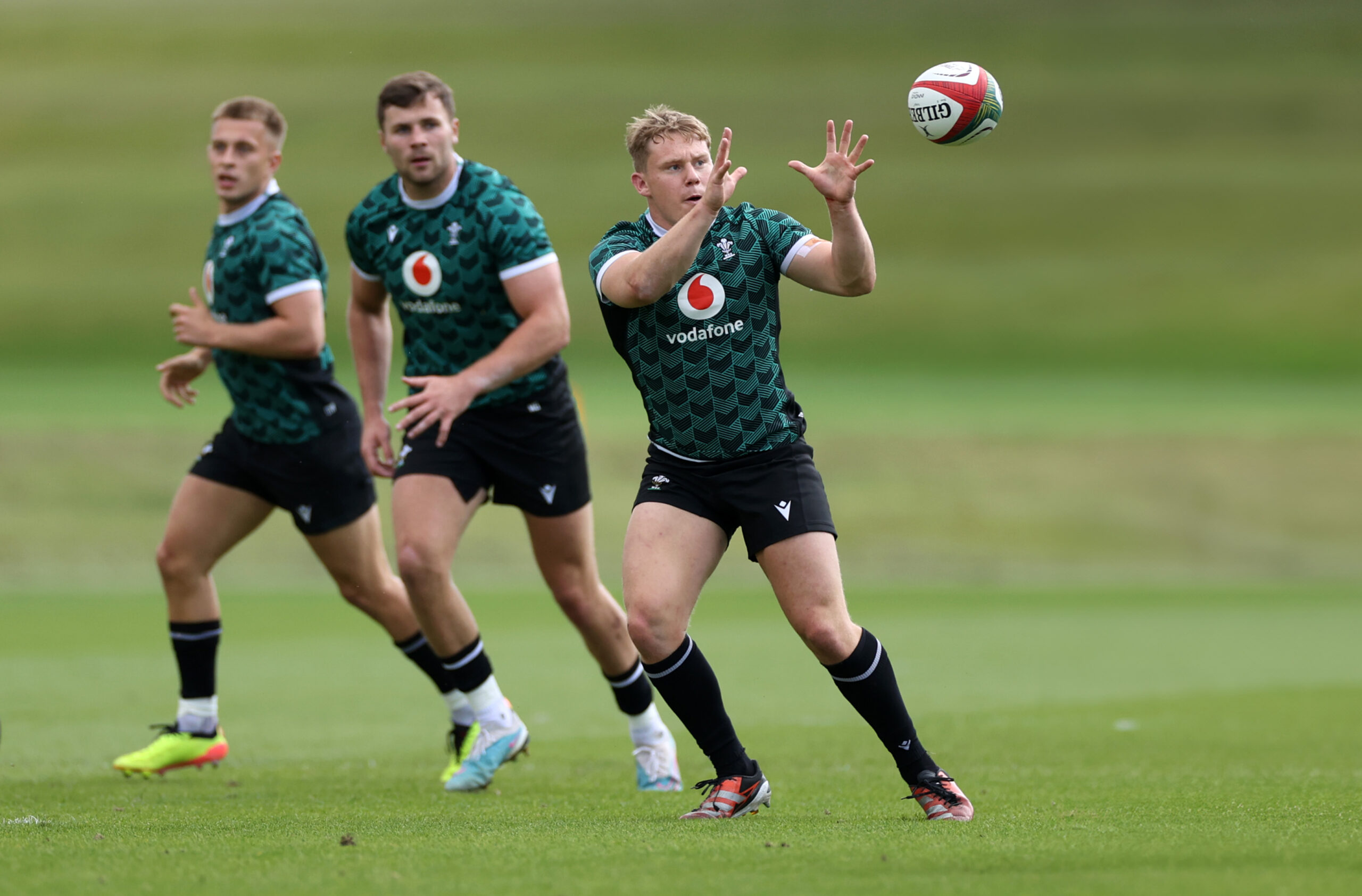 Three rugby players in green jerseys practicing on a field, with one catching a ball.