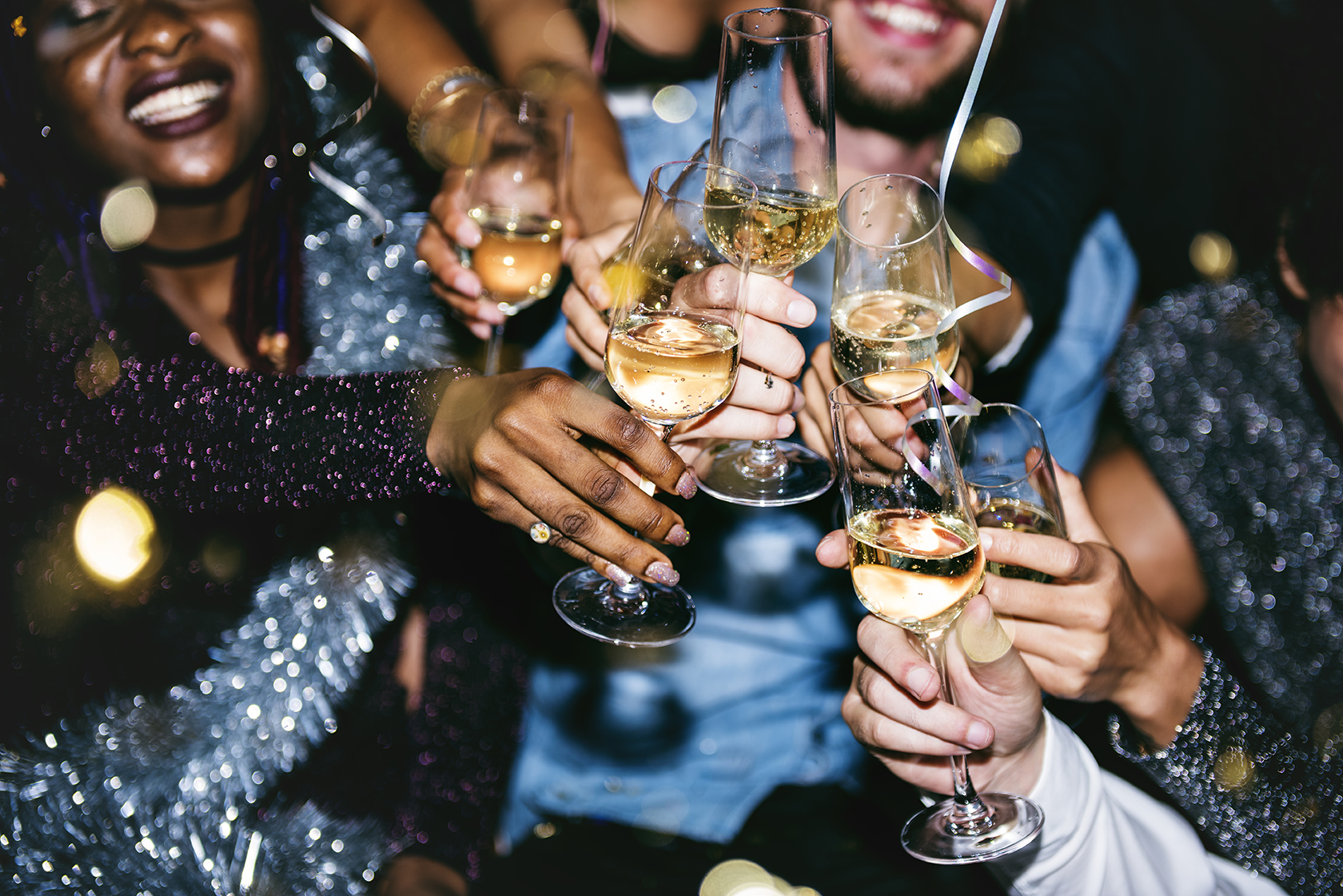 A group of people clinking glasses filled with champagne at a party, with festive attire and decorations visible.