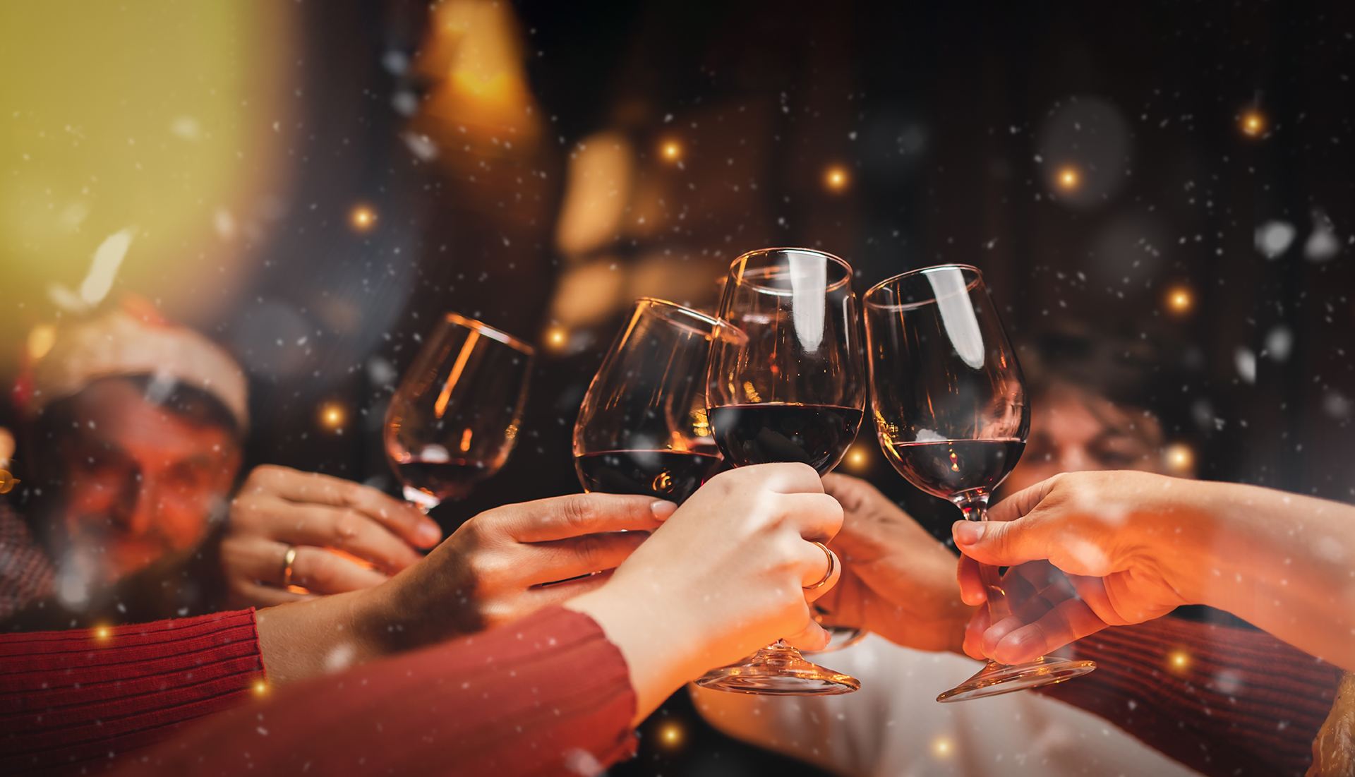 A group of people raise wine glasses in a celebratory toast, with a cozy, festive atmosphere and golden bokeh lights in the background.