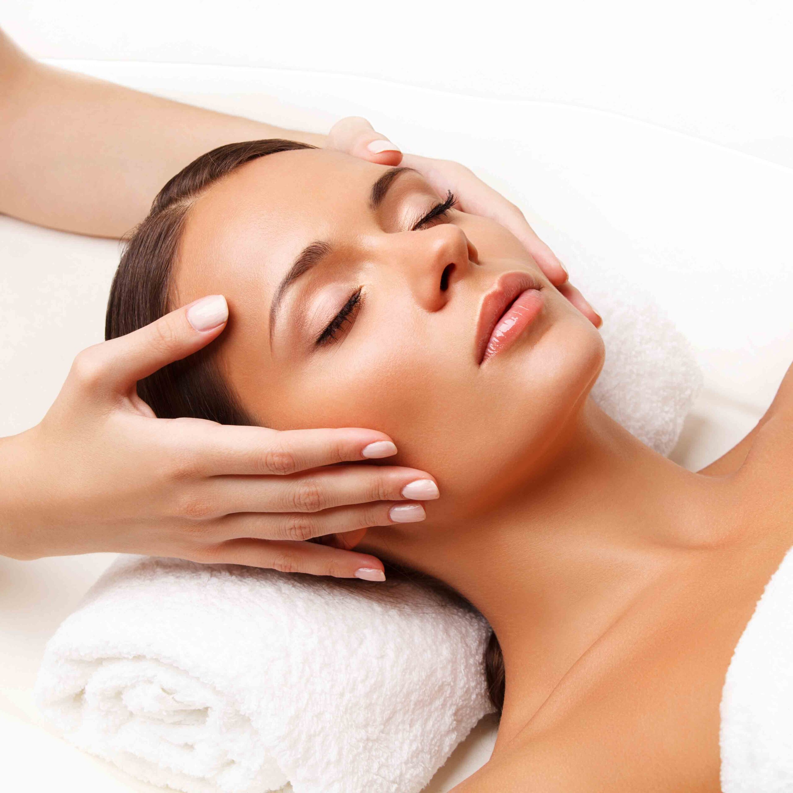 Person receiving a facial massage, lying on a white towel, with hands gently holding their head.