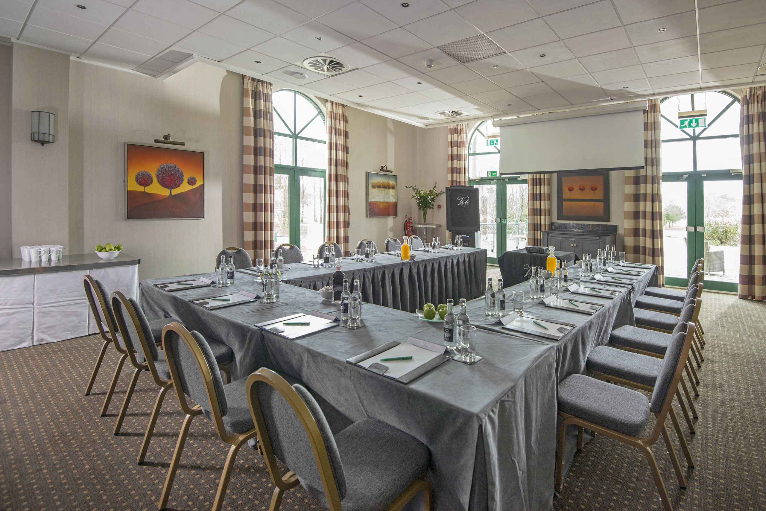 A conference room with a U-shaped table arrangement, chairs, water bottles, notepads, and decorative paintings on the walls.