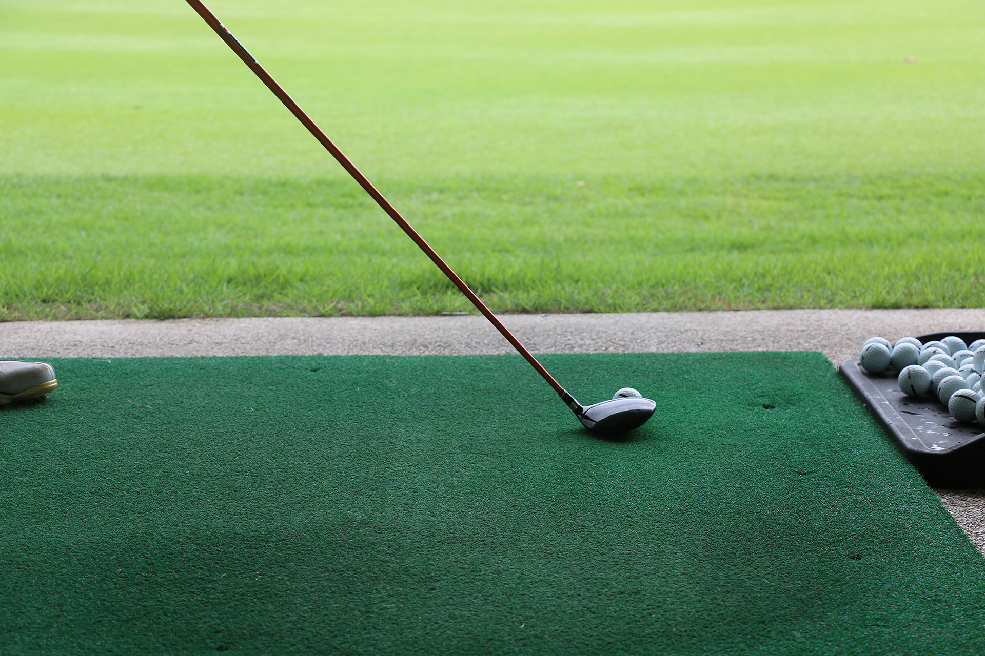 A golf club prepares to hit a ball on a driving range, with a stack of golf balls nearby on green turf.