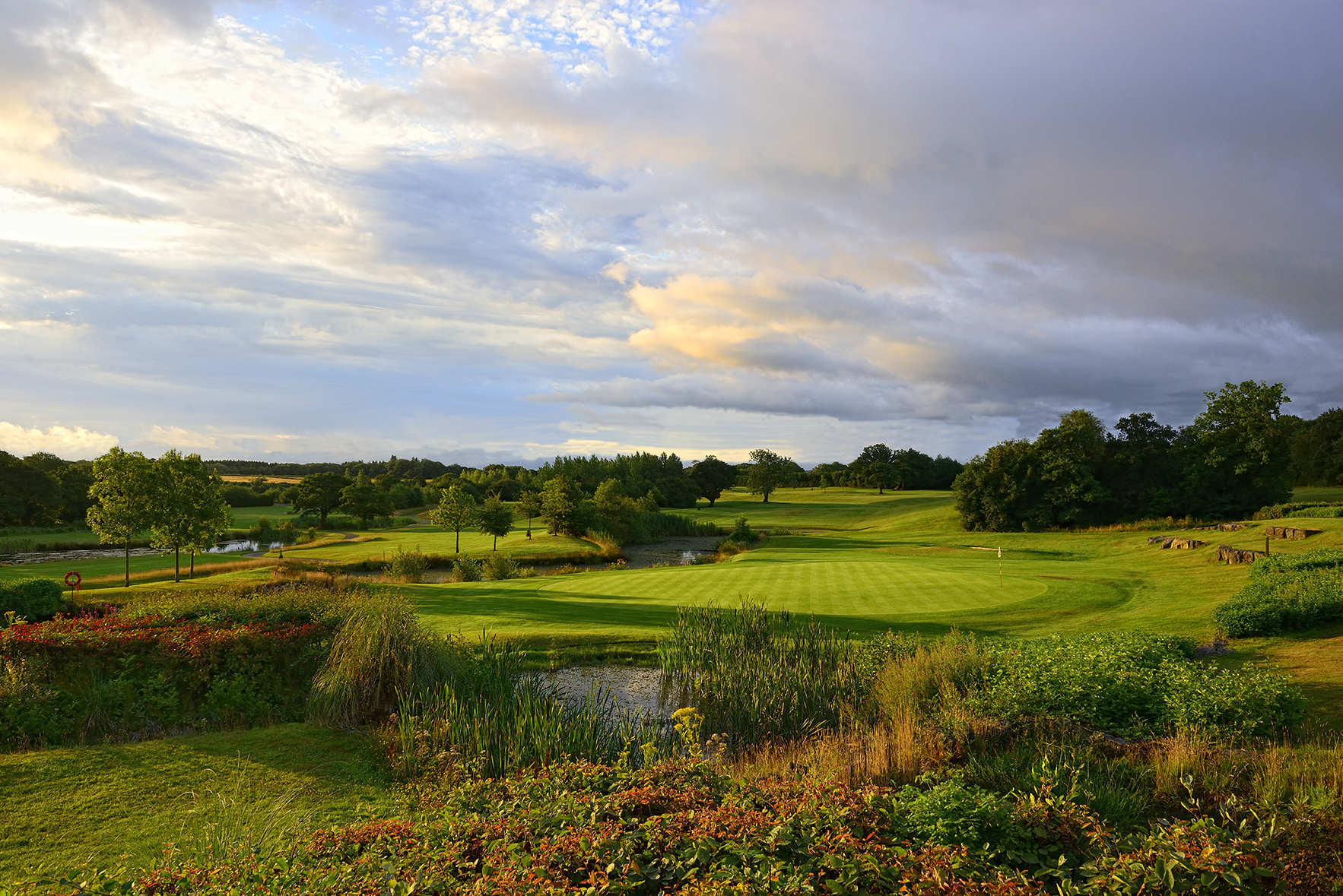 A scenic view of a golf course with a green lawn, trees, and a partly cloudy sky in the background.