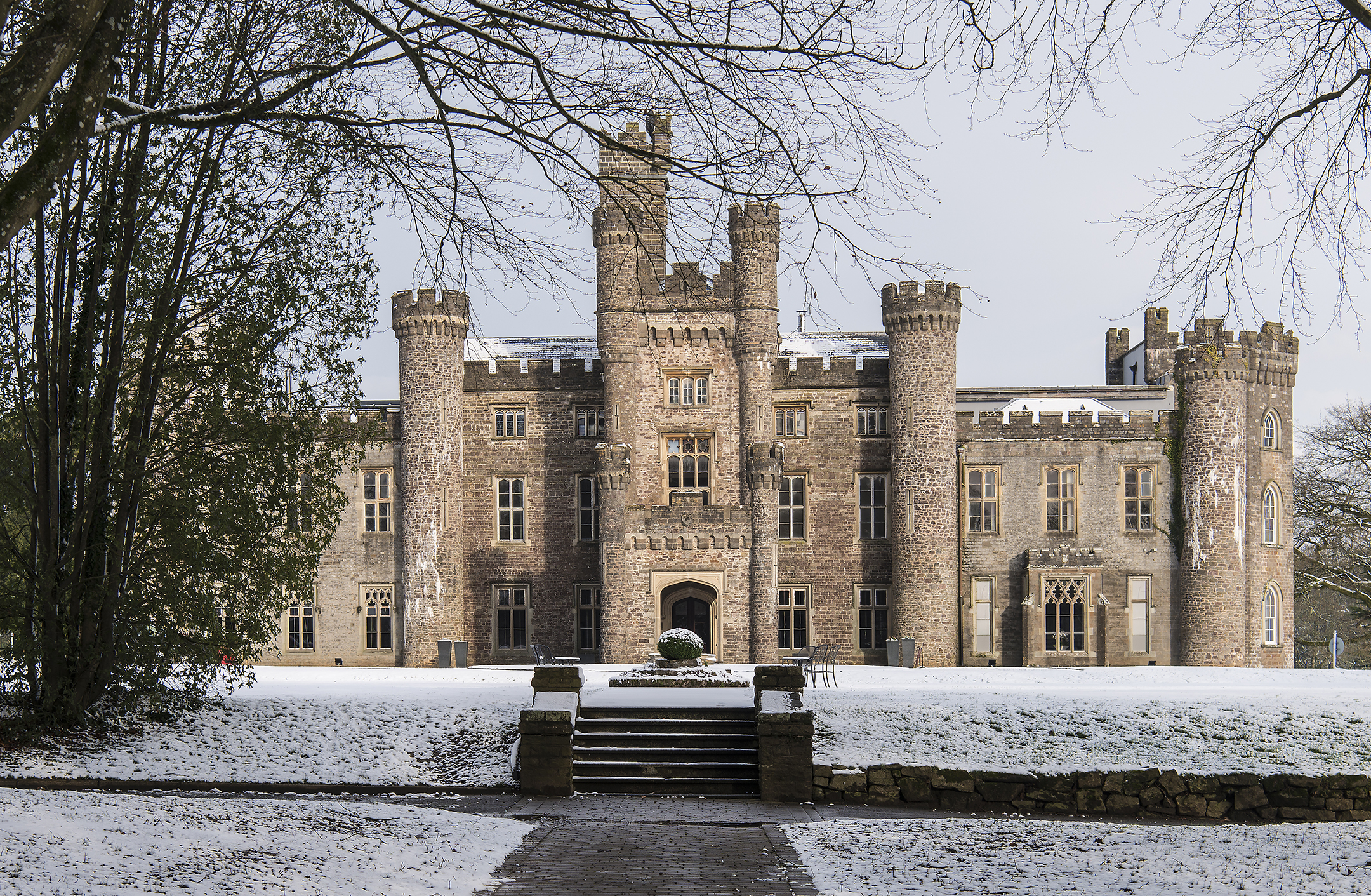 A large stone castle with multiple turrets is surrounded by a snowy landscape and bare trees.