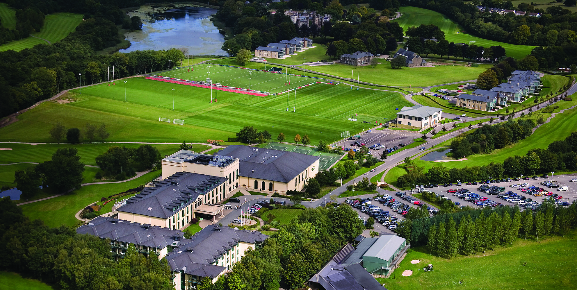 Aerial view of a sports complex with multiple fields surrounded by buildings, parking lots, and greenery.