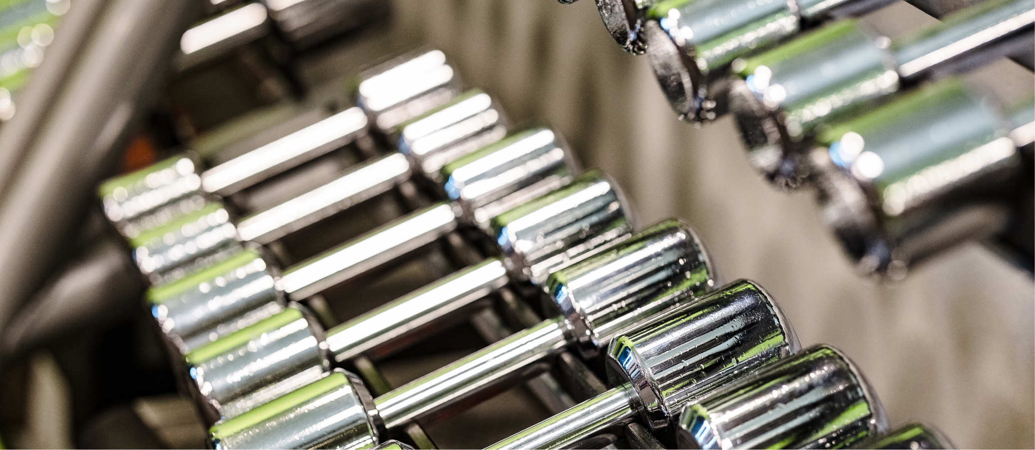 Close-up of rows of chrome dumbbells on a rack in a gym.