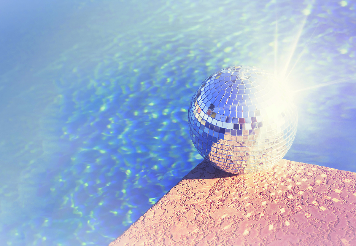 A disco ball sits on the edge of a textured surface, reflecting sunlight, with a bright blue pool in the background.