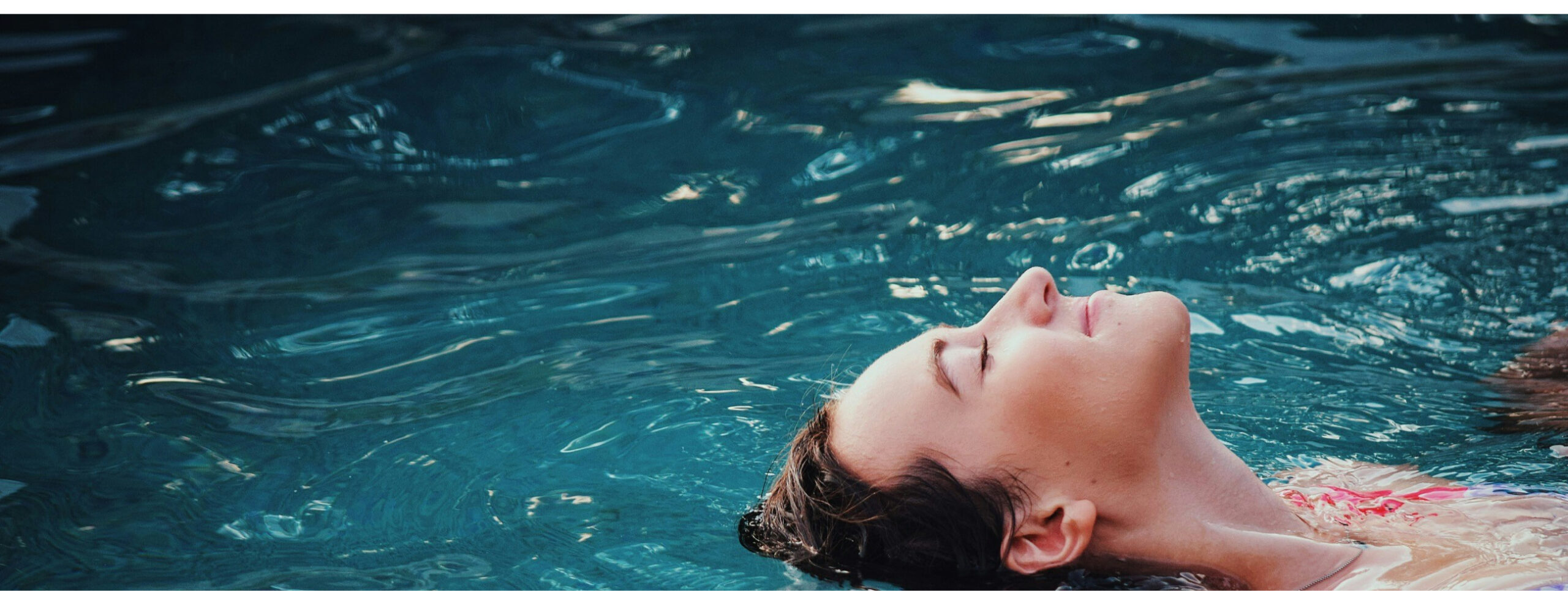 A person floating peacefully in a swimming pool, eyes closed, with water gently rippling around them.