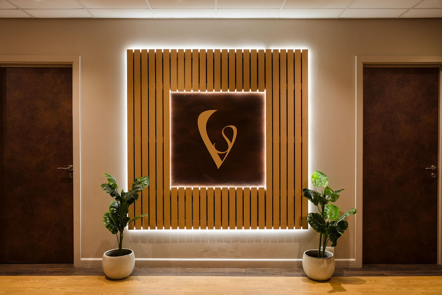 A wall display features a stylized logo on a lit panel, flanked by two doors and two potted plants.