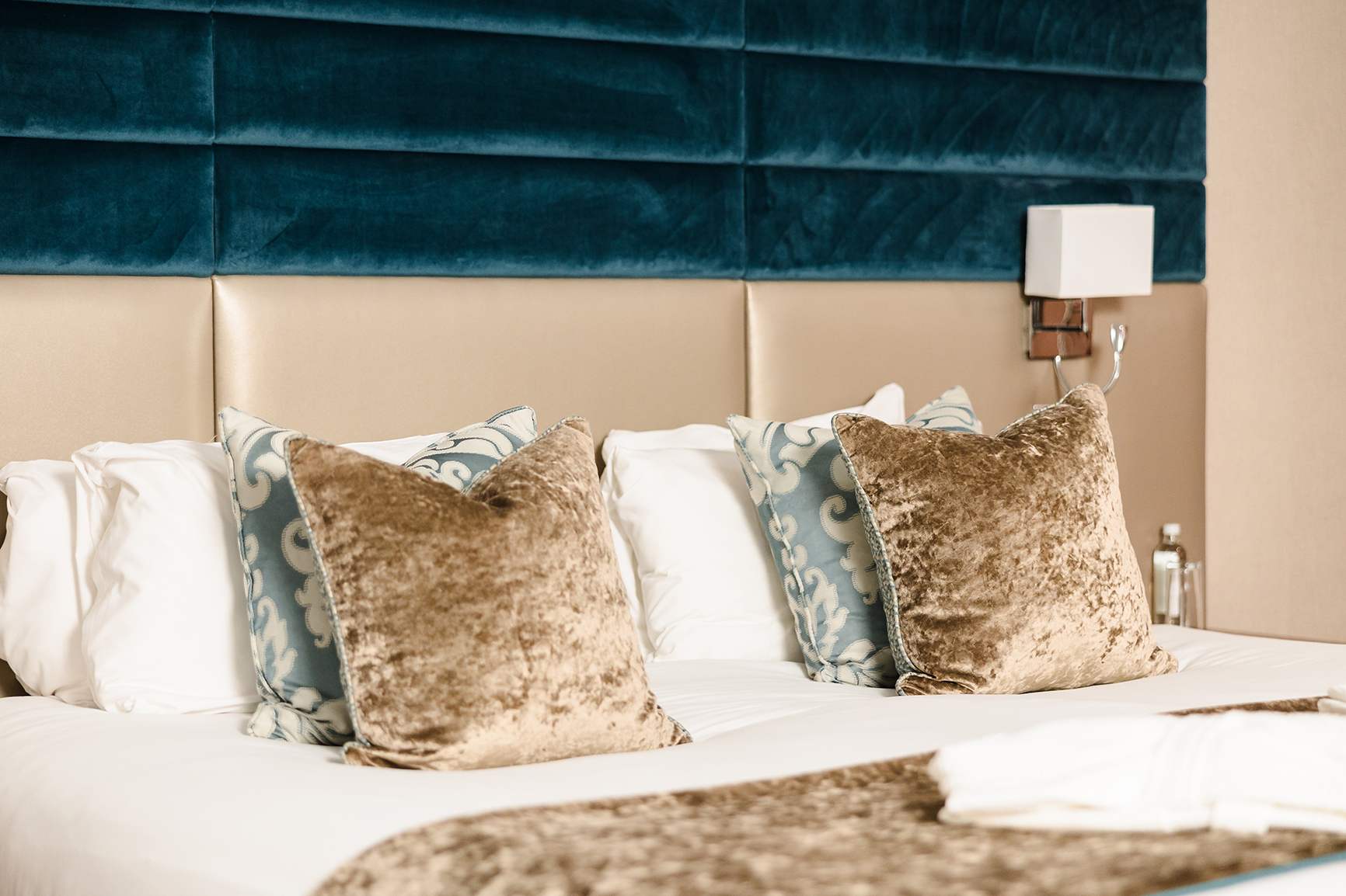 A neatly made bed with decorative pillows and a plush headboard, featuring a mix of textures and patterns in blue and beige tones.