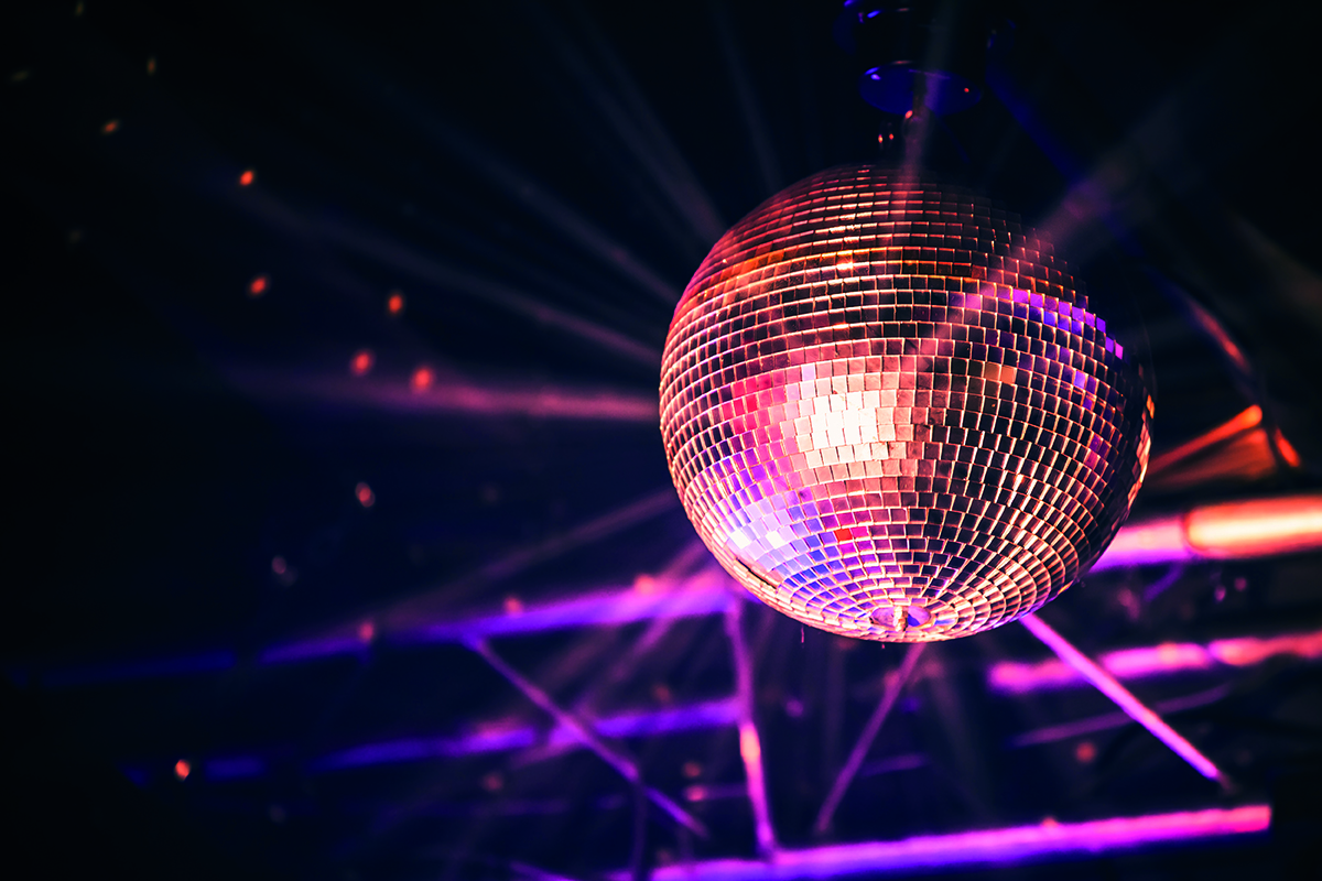 A glowing disco ball hangs from the ceiling, reflecting colorful lights in a dark room.