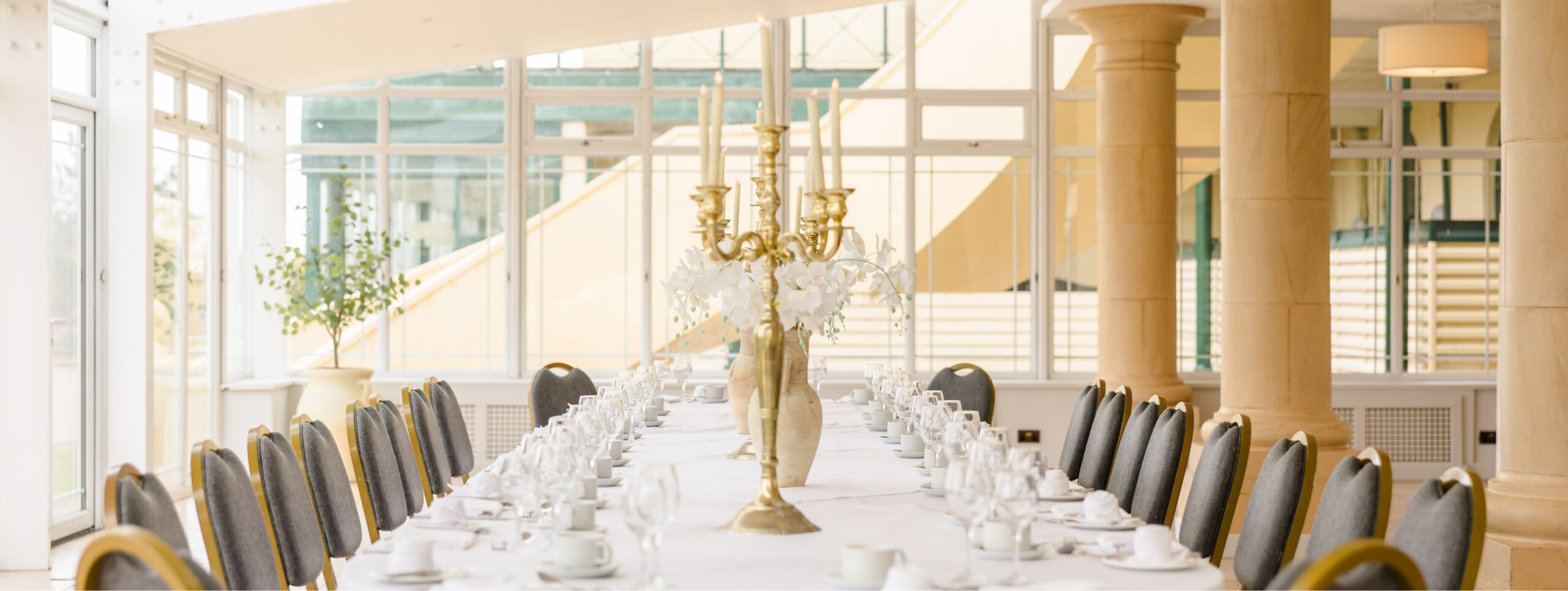 Elegant dining room with a long table set with white tablecloth, fine china, and a gold candelabra centerpiece.