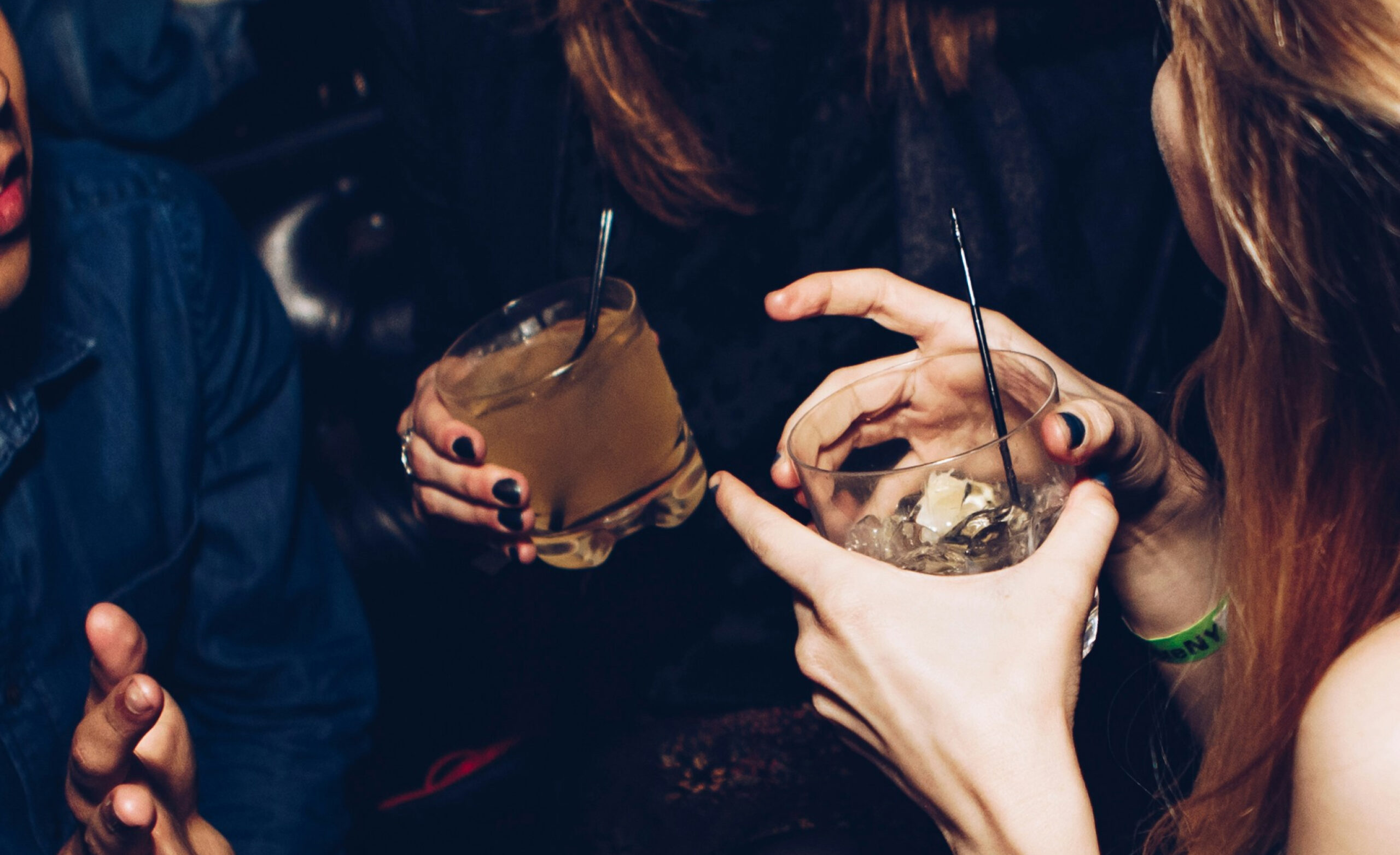 Three people are holding drinks with straws in a dimly lit setting.