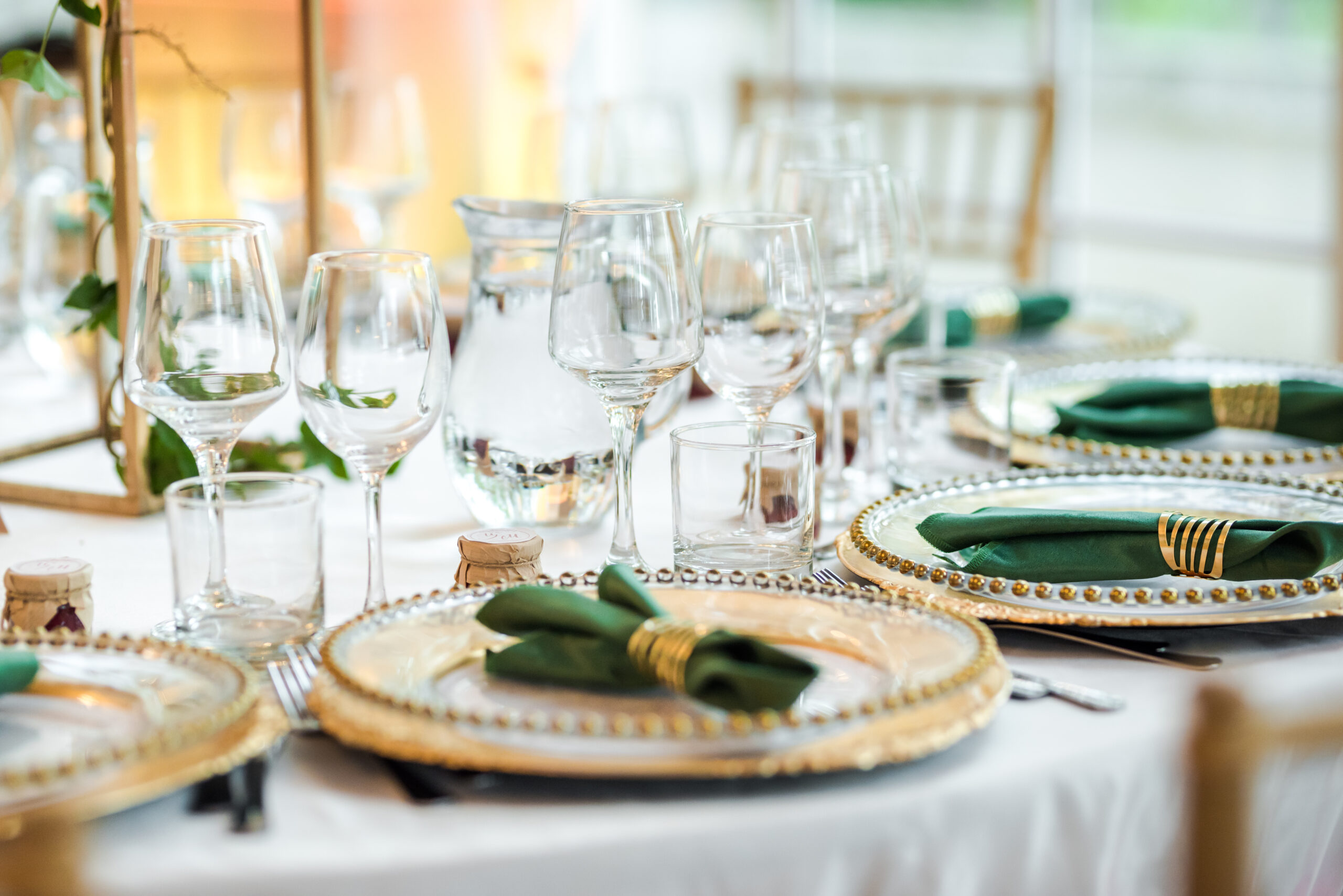 Elegant table setting with glassware, gold-trimmed plates, and green napkins on a white tablecloth.