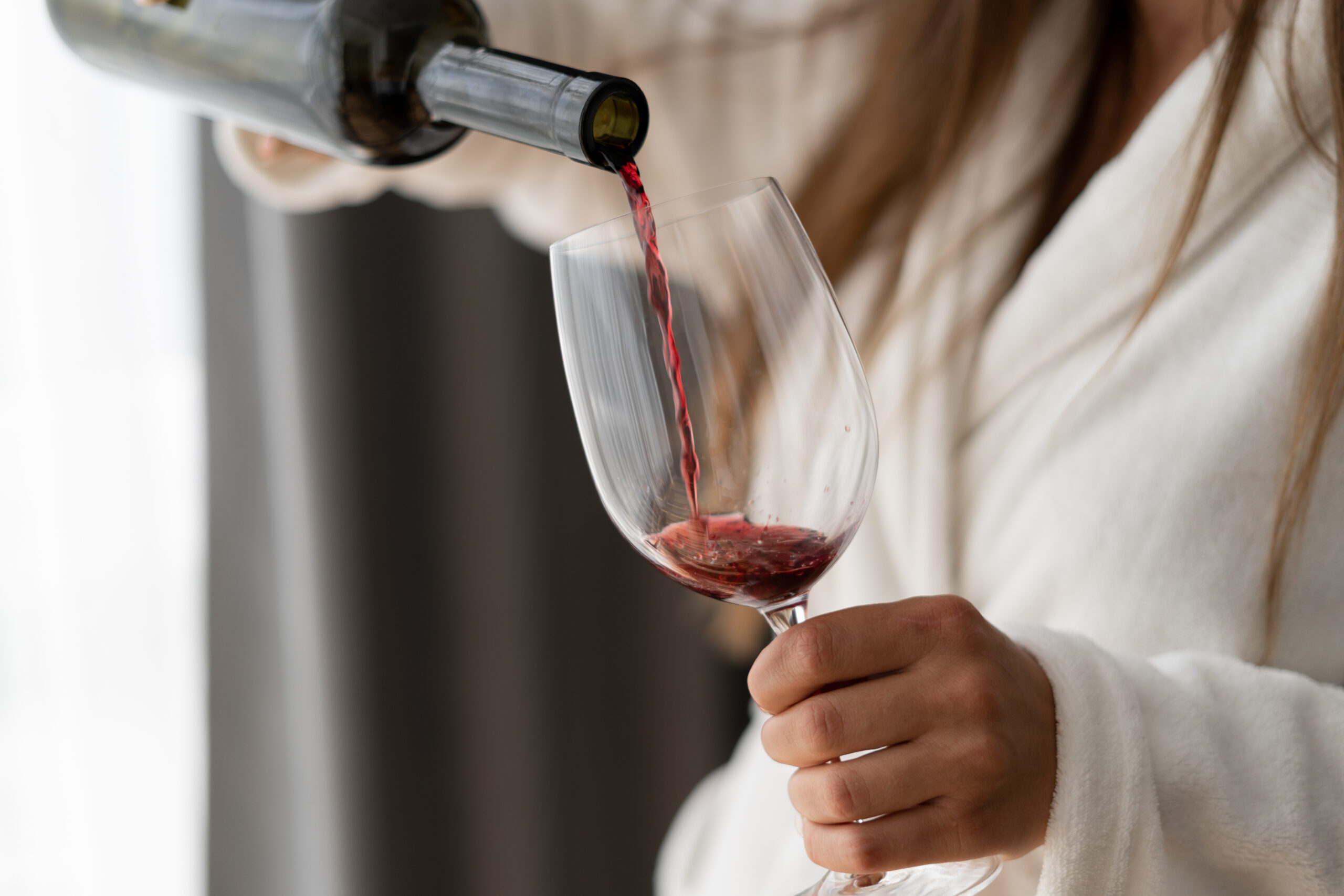 A person in a white robe pours red wine into a wine glass.