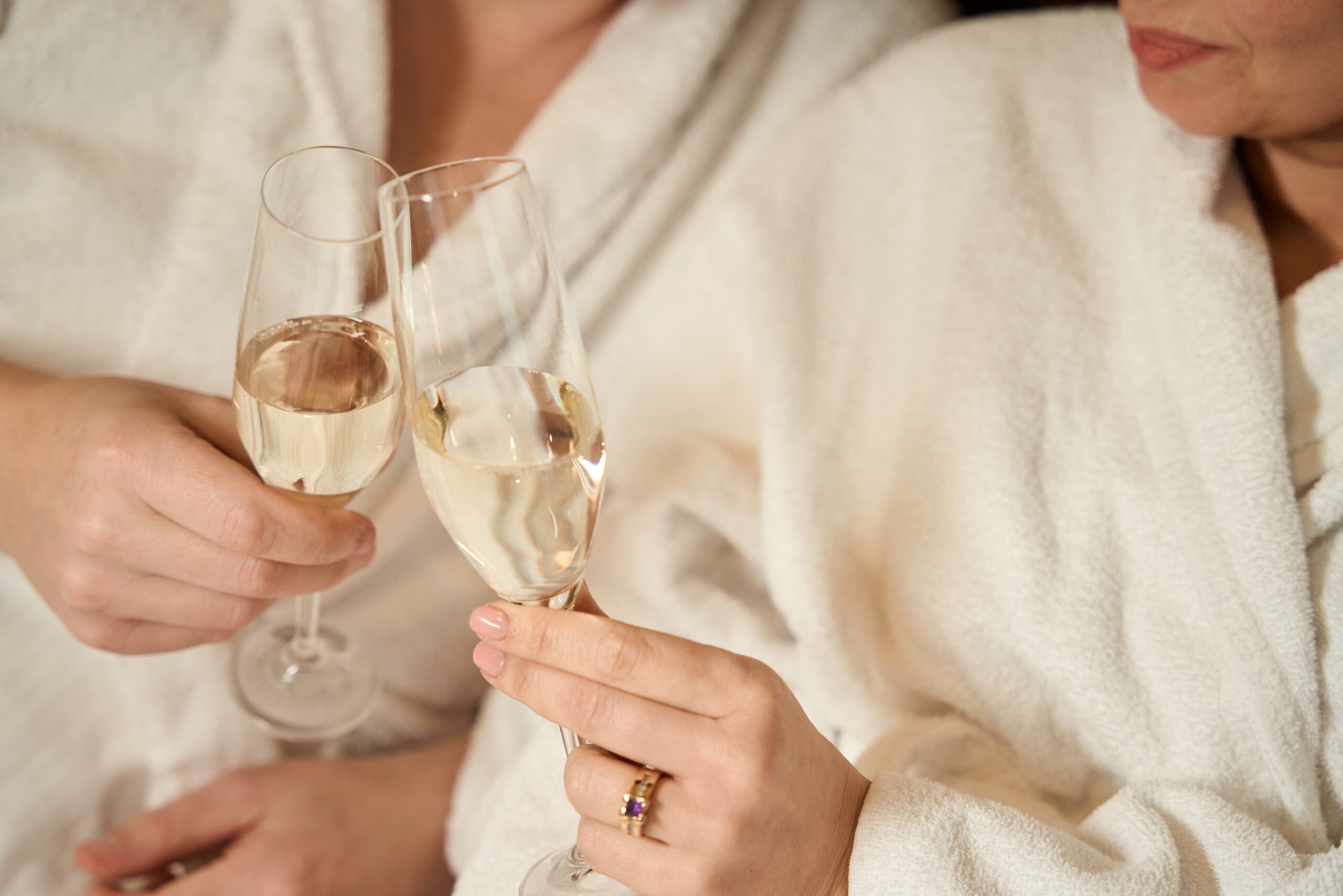 Two people in white robes clink glasses of champagne.