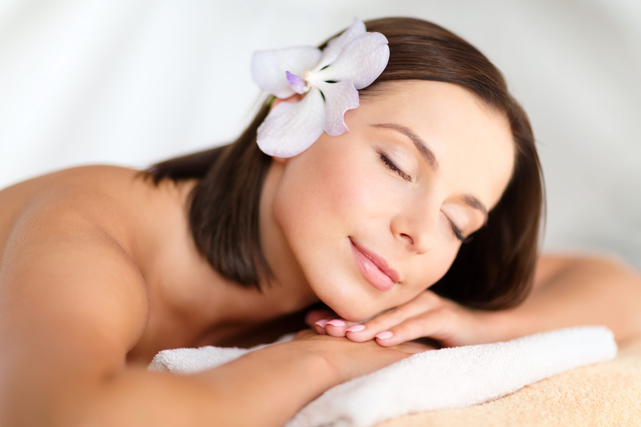 A woman with closed eyes rests her head on folded arms, with a white flower tucked in her hair.