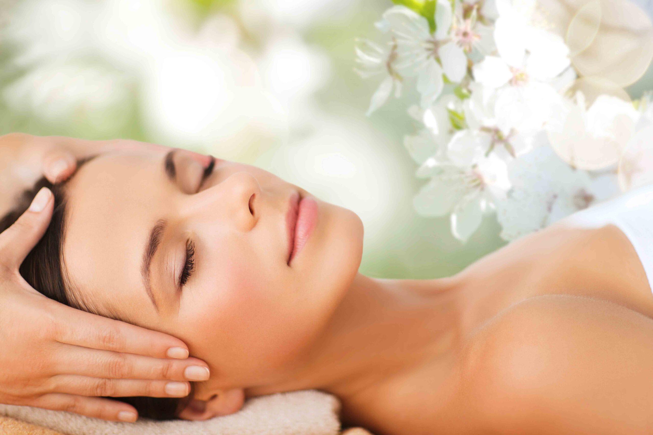 A person receives a relaxing head massage, surrounded by white flowers, with eyes closed.