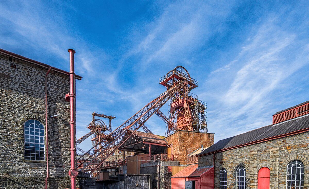 Industrial site with brick buildings and two red metal mining structures against a blue sky.