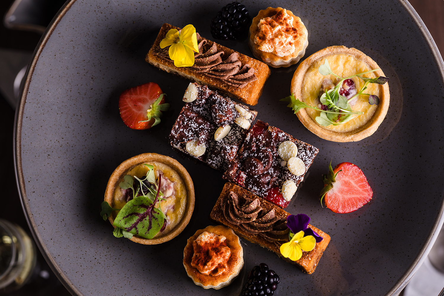 A plate of assorted desserts, including tarts, chocolate pastries, and fresh berries, garnished with edible flowers.