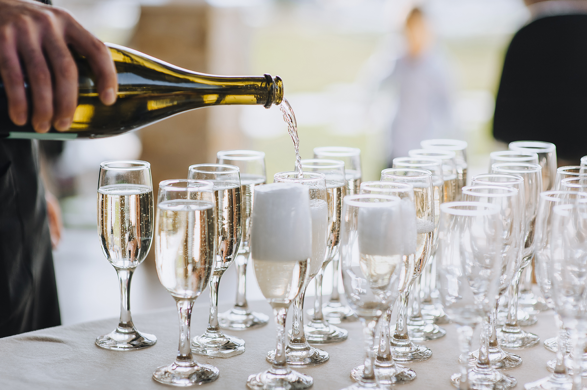 A person pours champagne into multiple glasses arranged on a table.