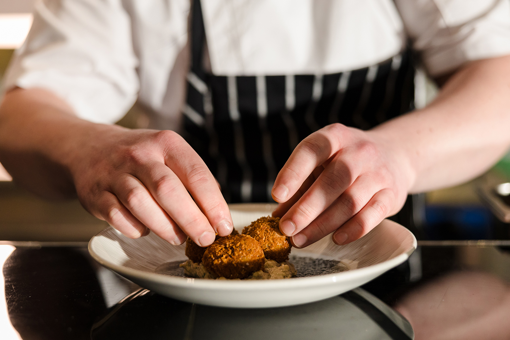 Chef plating crispy croquettes on a white dish.