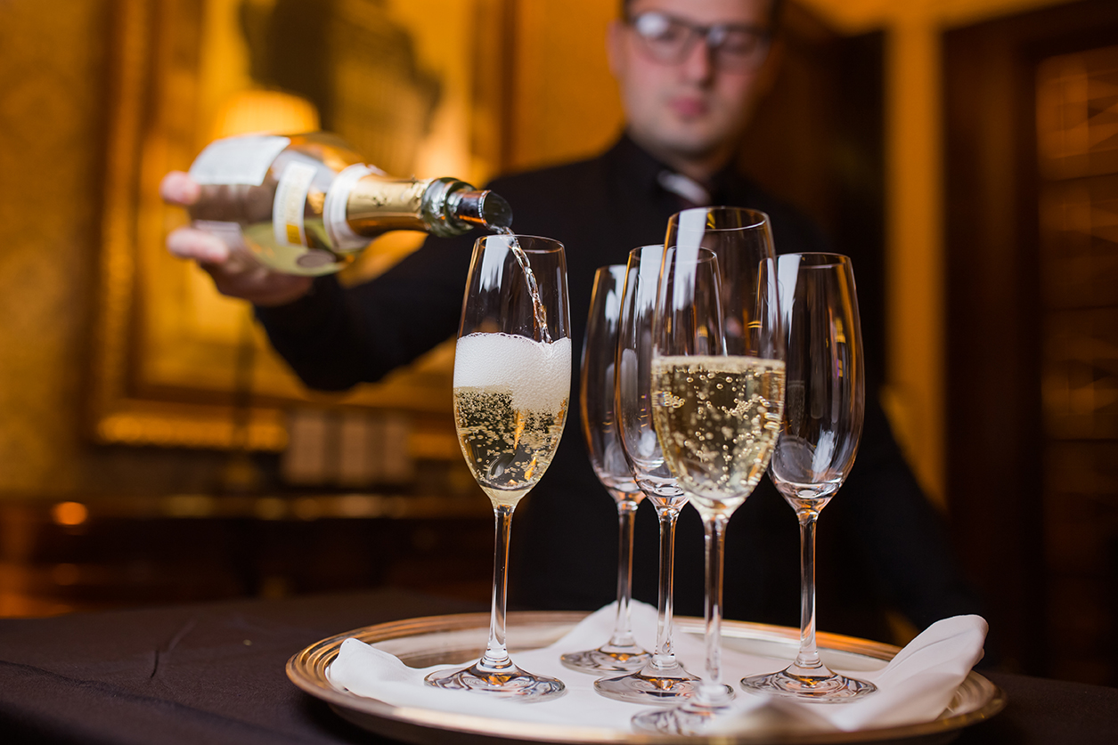 A waiter pours champagne into flutes on a tray, ready for serving.