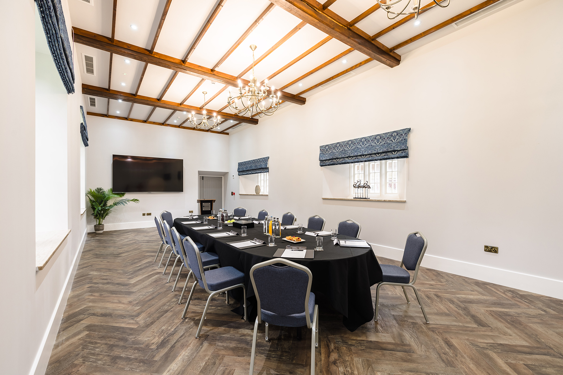 A conference room with a long table set up with chairs, notepads, and water bottles, featuring a large screen and chandeliers.