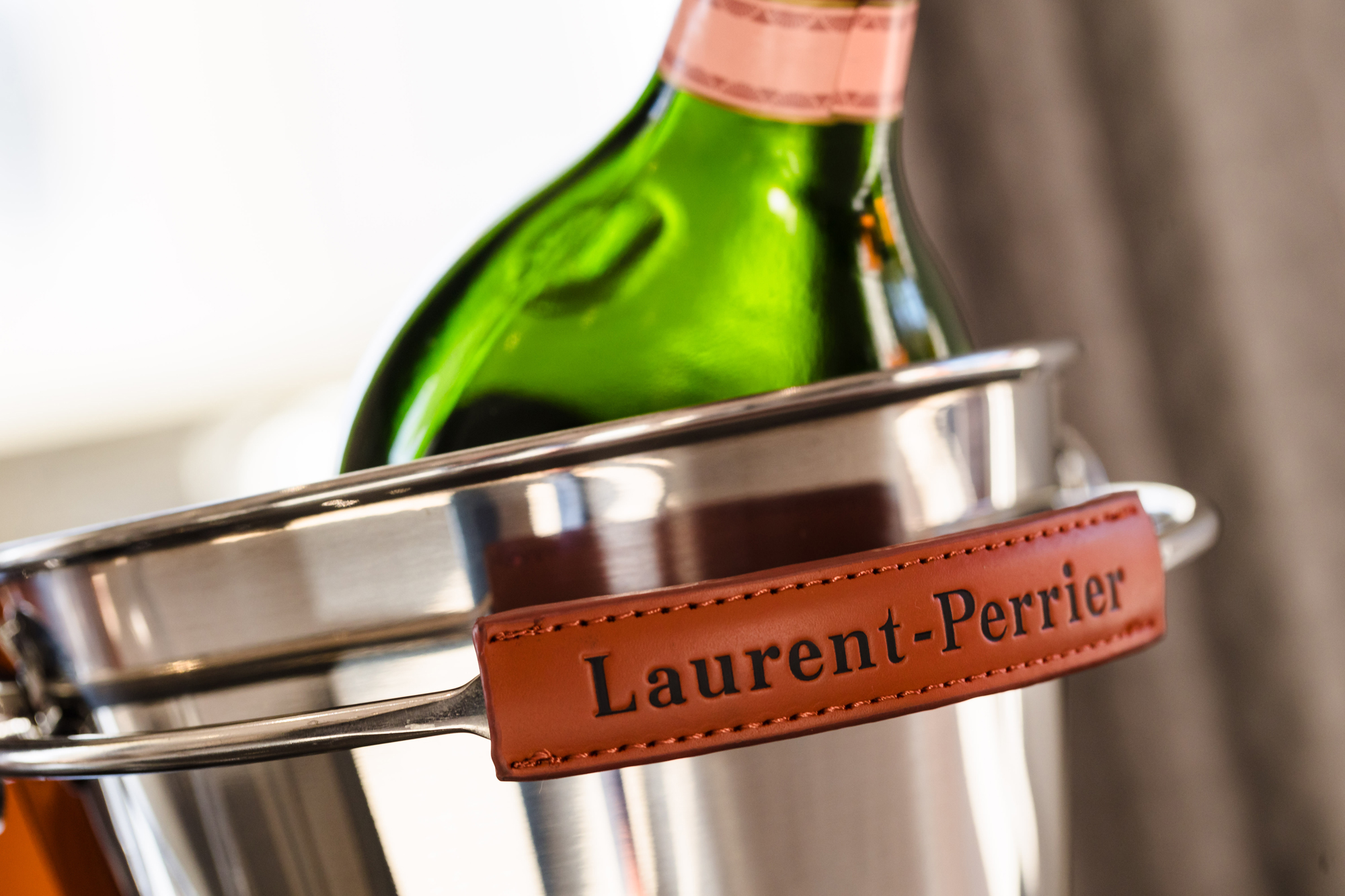 Close-up of a Laurent-Perrier bottle resting in a metal ice bucket with a leather label on a blurred background.